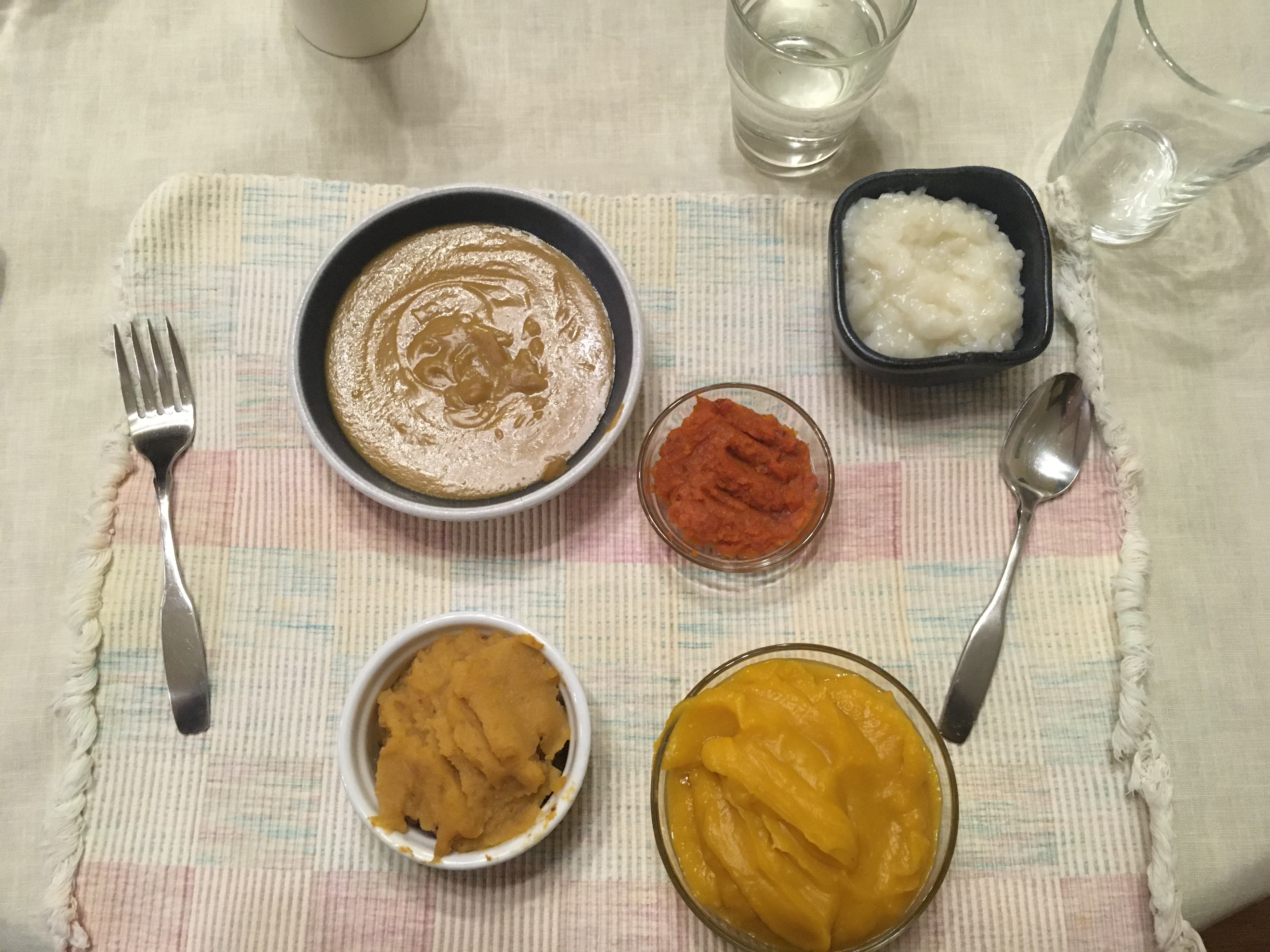 White placemat with 5 small bowls of pureed foods in different shades of orange/brown/white.