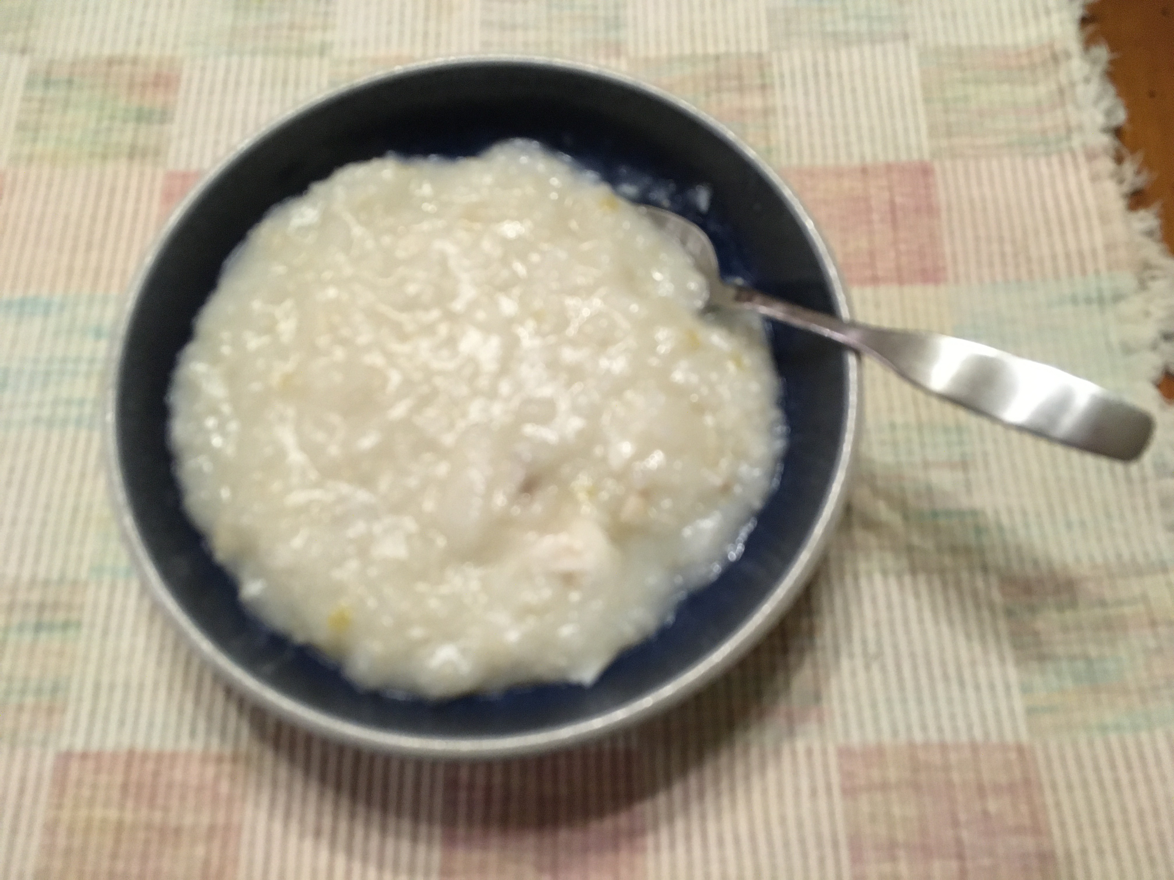 Photo of blue bowl, with white jook and a spoon, on a white checkerboard placemat.